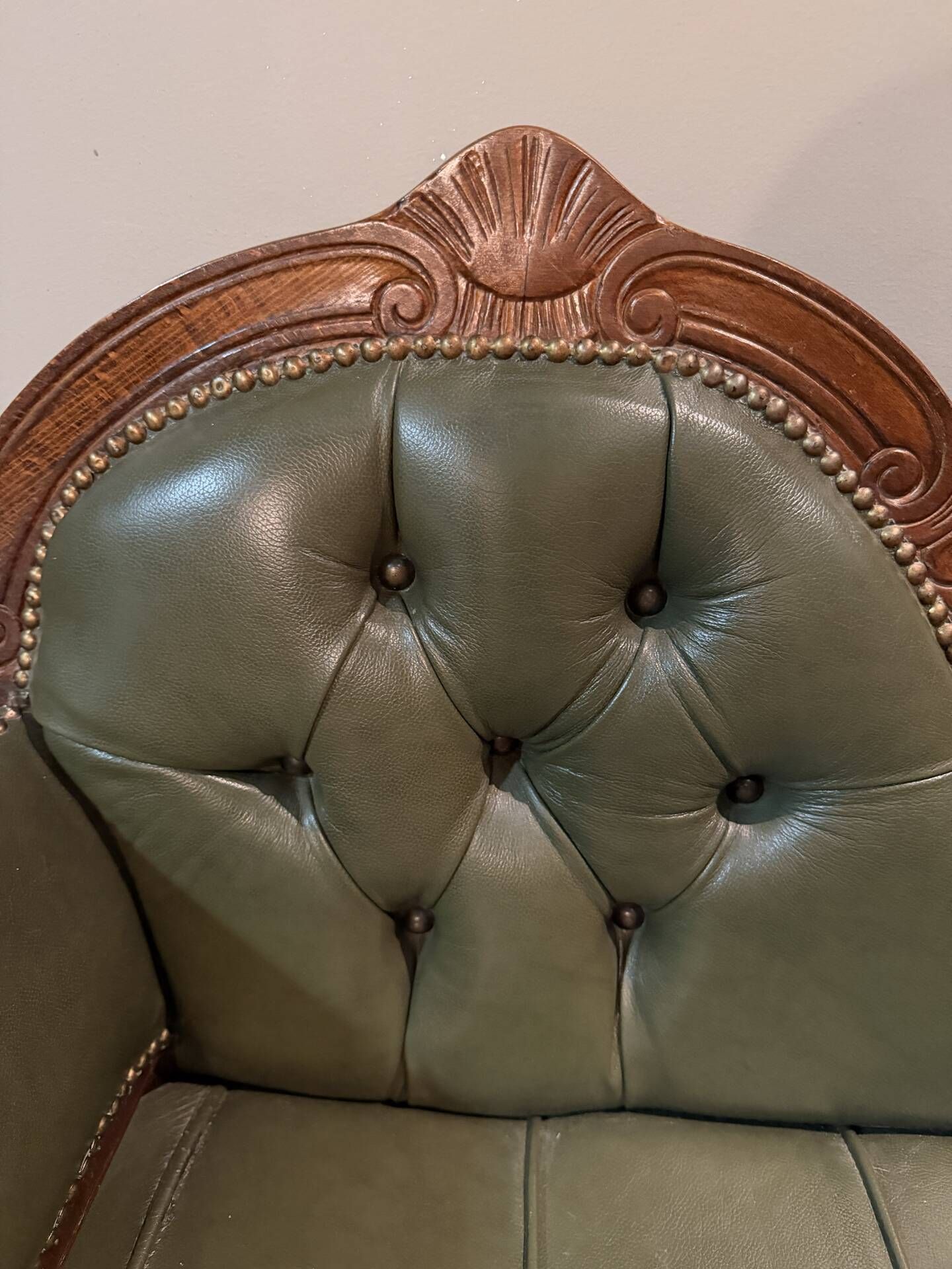 Antique carved wooden bench with green upholstered seat and backrest.