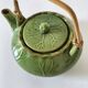 Vintage green teapot with lotus decoration and bamboo handle.