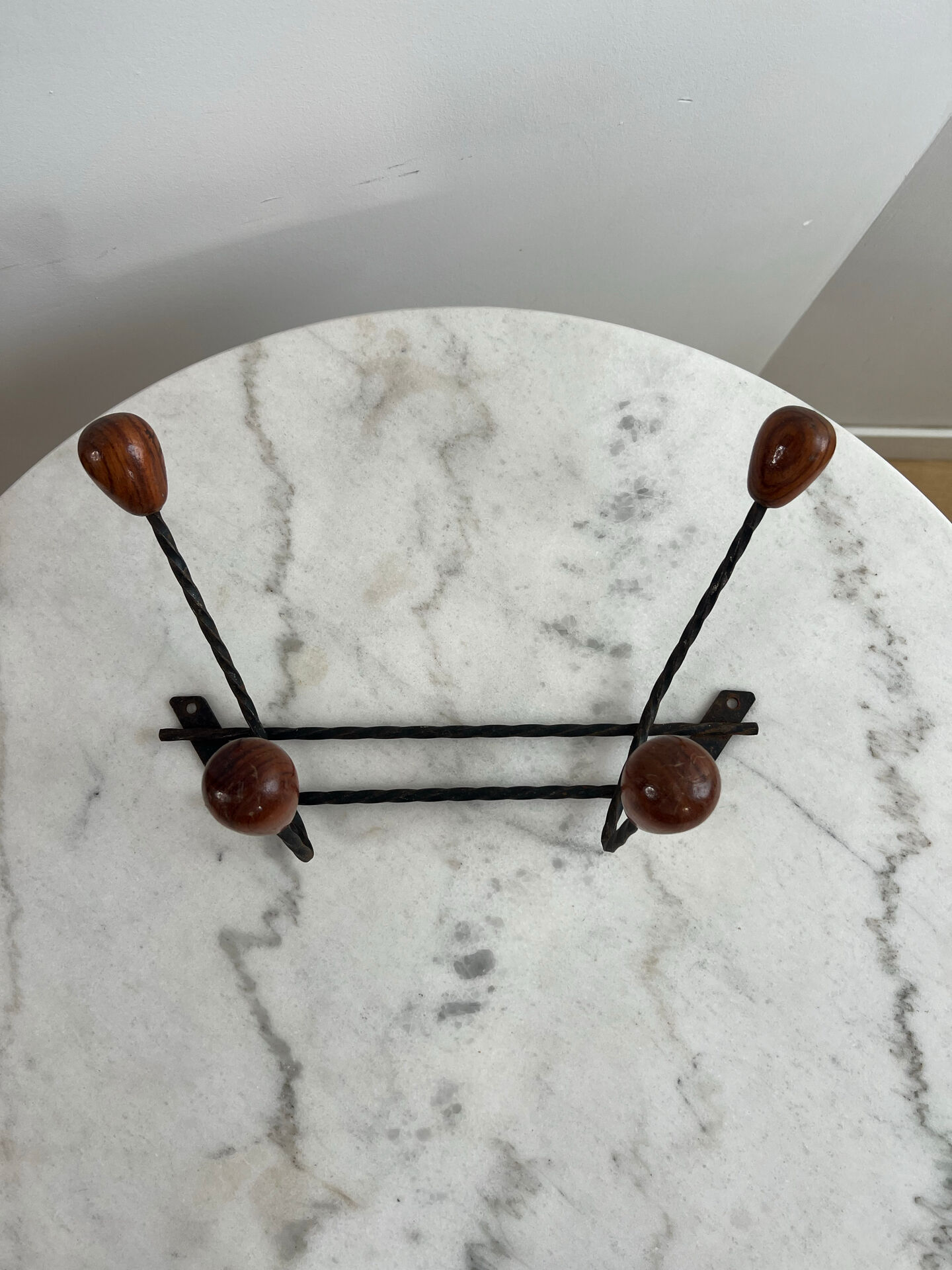 Wall-mounted coat rack in wrought iron with turned wooden knobs.