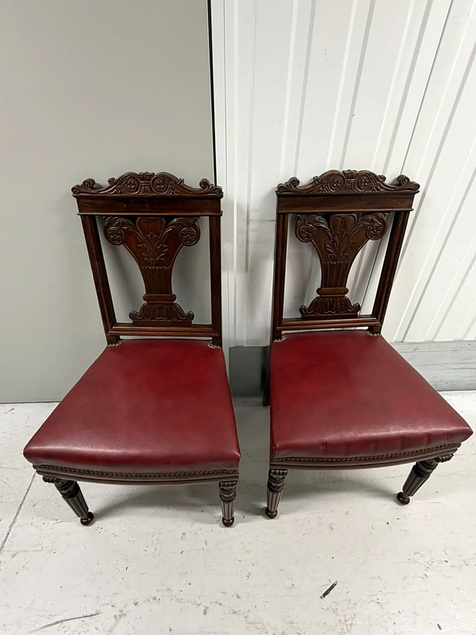 Pair of carved mahogany chairs with red faux leather seats.