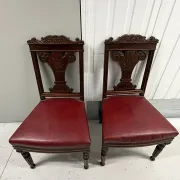 Pair of carved mahogany chairs with red faux leather seats.