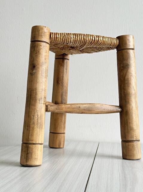 Antique tripod stool in light wood with a woven straw seat.