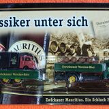 Mercedes flatbed containing drums pulling 1 trailer carrying 1 covered vehicle