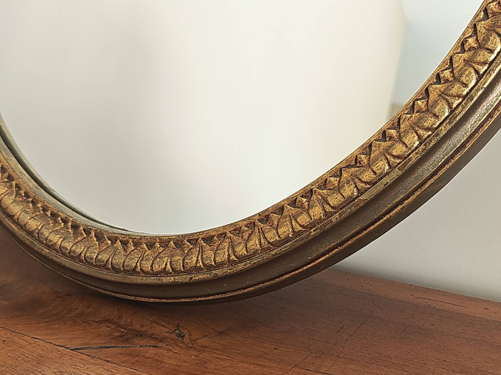 Vintage oval mirror with a carved wooden frame in gold, decorated with a bow.