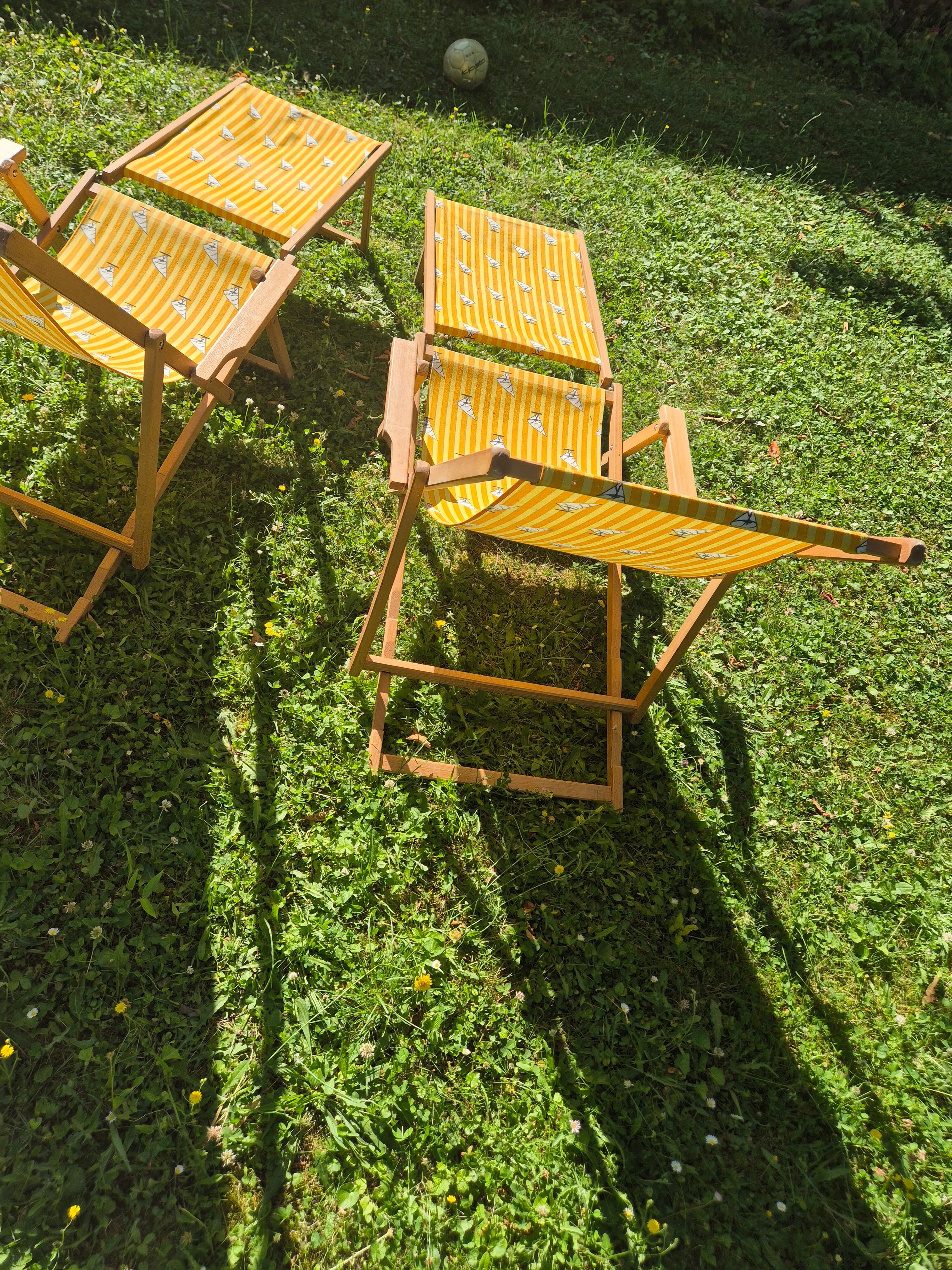 2 vintage Chilean deck chairs made of wood and yellow fabric printed with sailboats, with footrests.