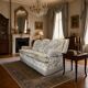Vintage beige three-seater sofa with floral pattern and fringes.