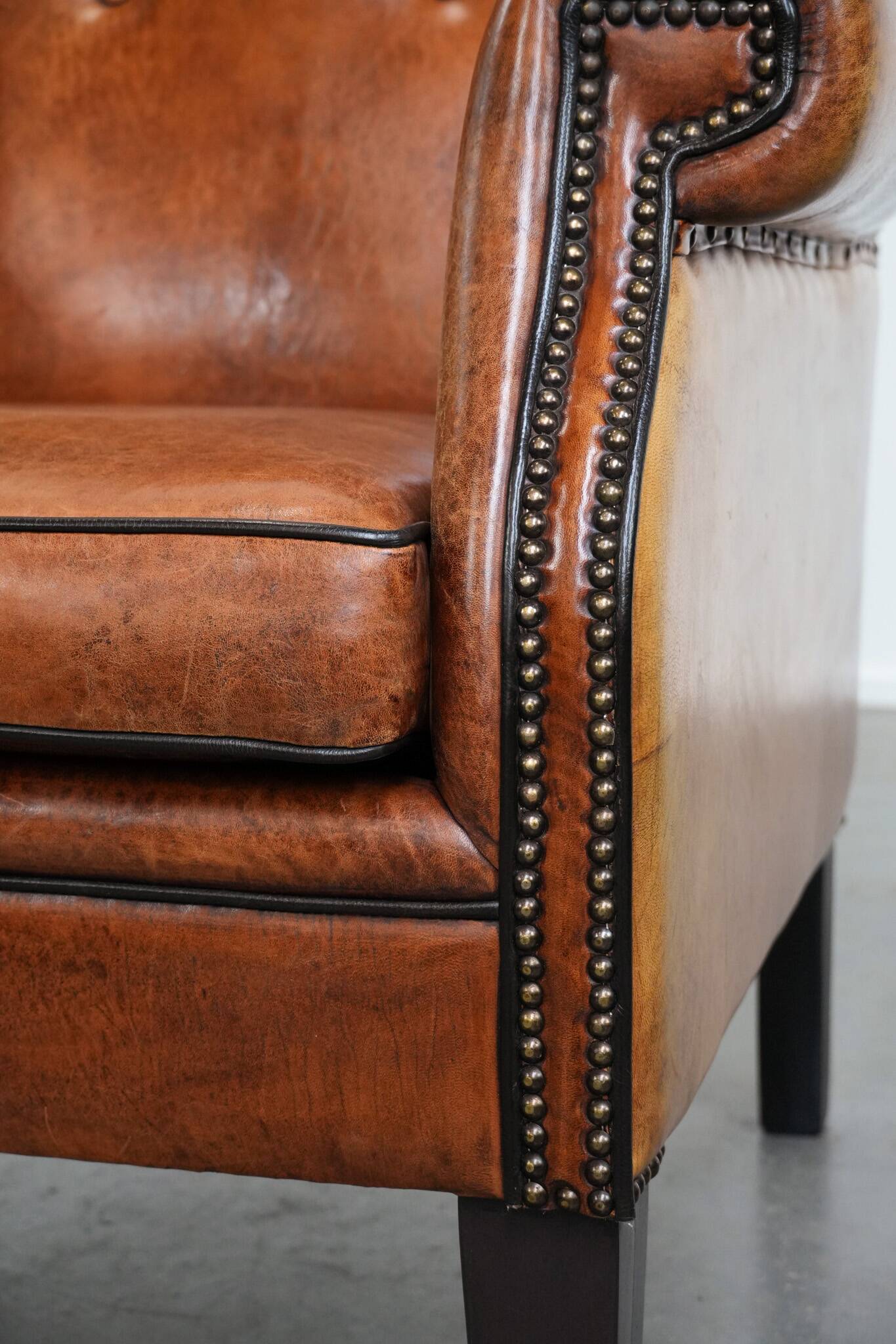 Large sheepskin wingback chair with black piping and decorative nails