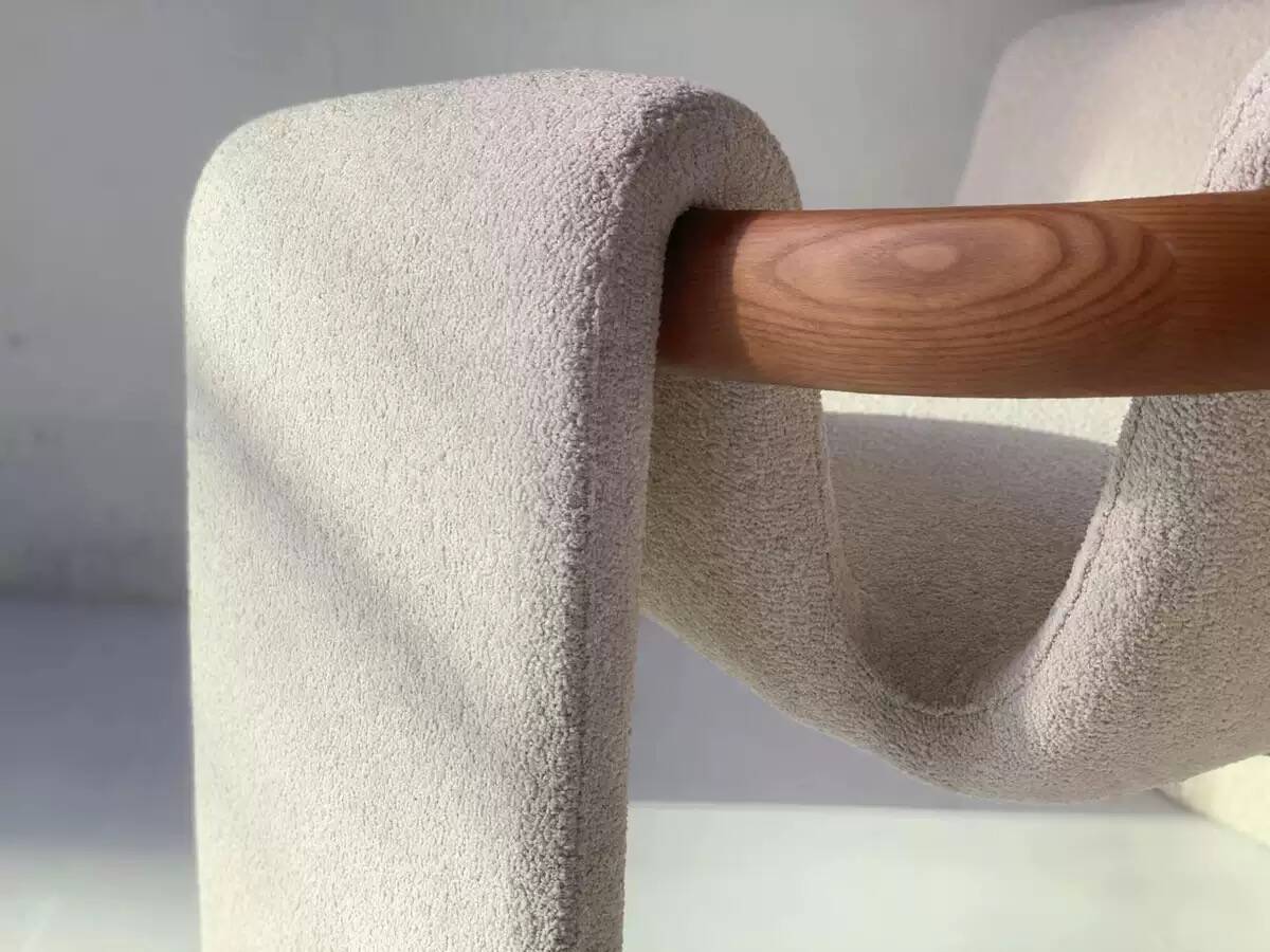 Sculptural lounge armchair in ecru boucle fabric with solid wood details.