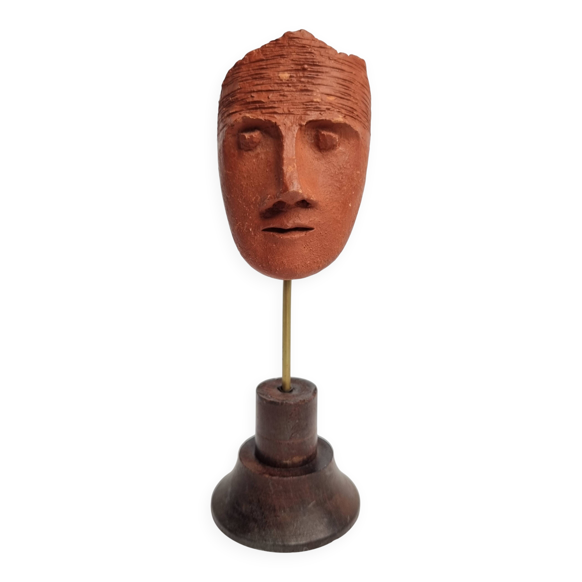 Stylized head in patinated ochre terracotta on a dark wooden base, 17 cm