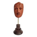 Stylized head in patinated ochre terracotta on a dark wooden base, 17 cm