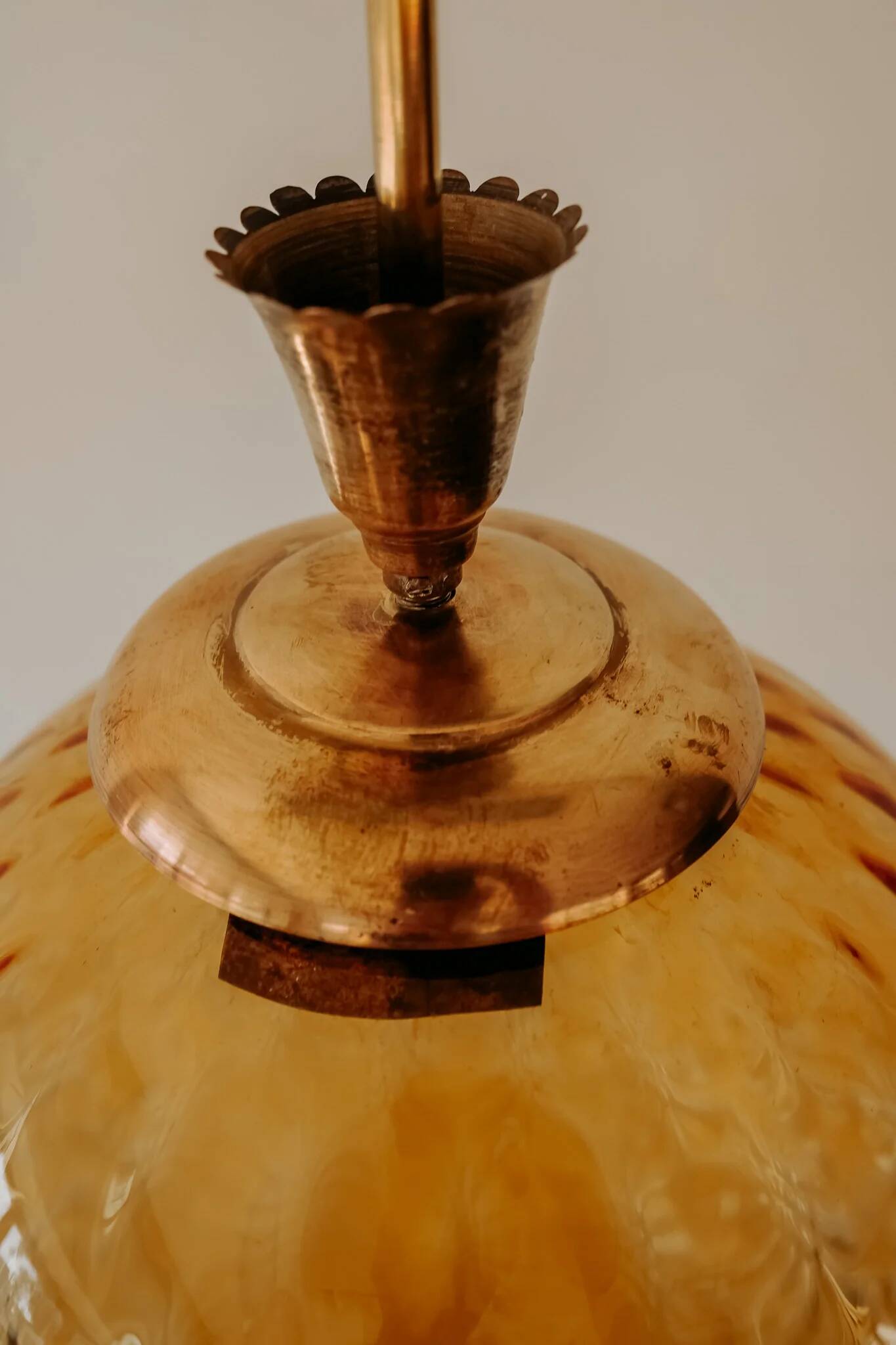 Brass pendant light with a round orange glass shade and a swirling structure.