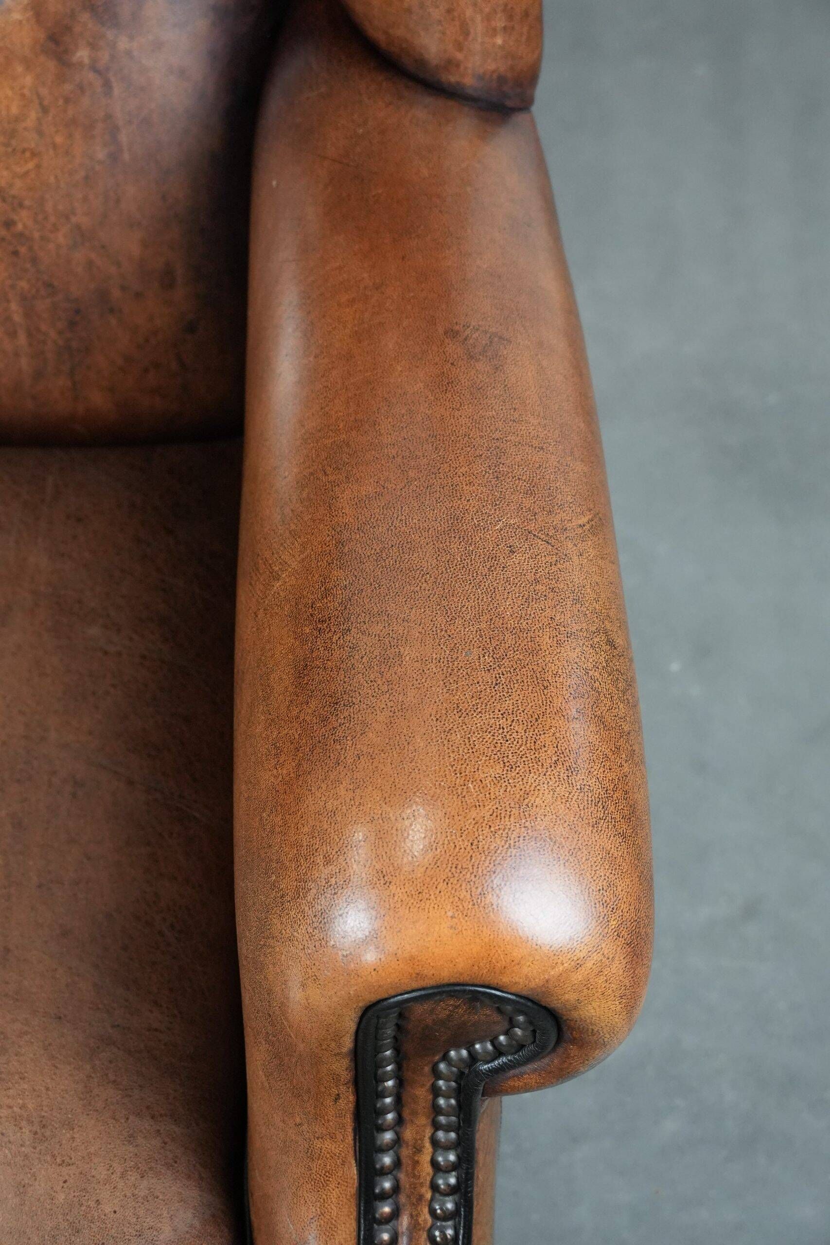 Sheepskin wingback armchair with decorative nails and black piping