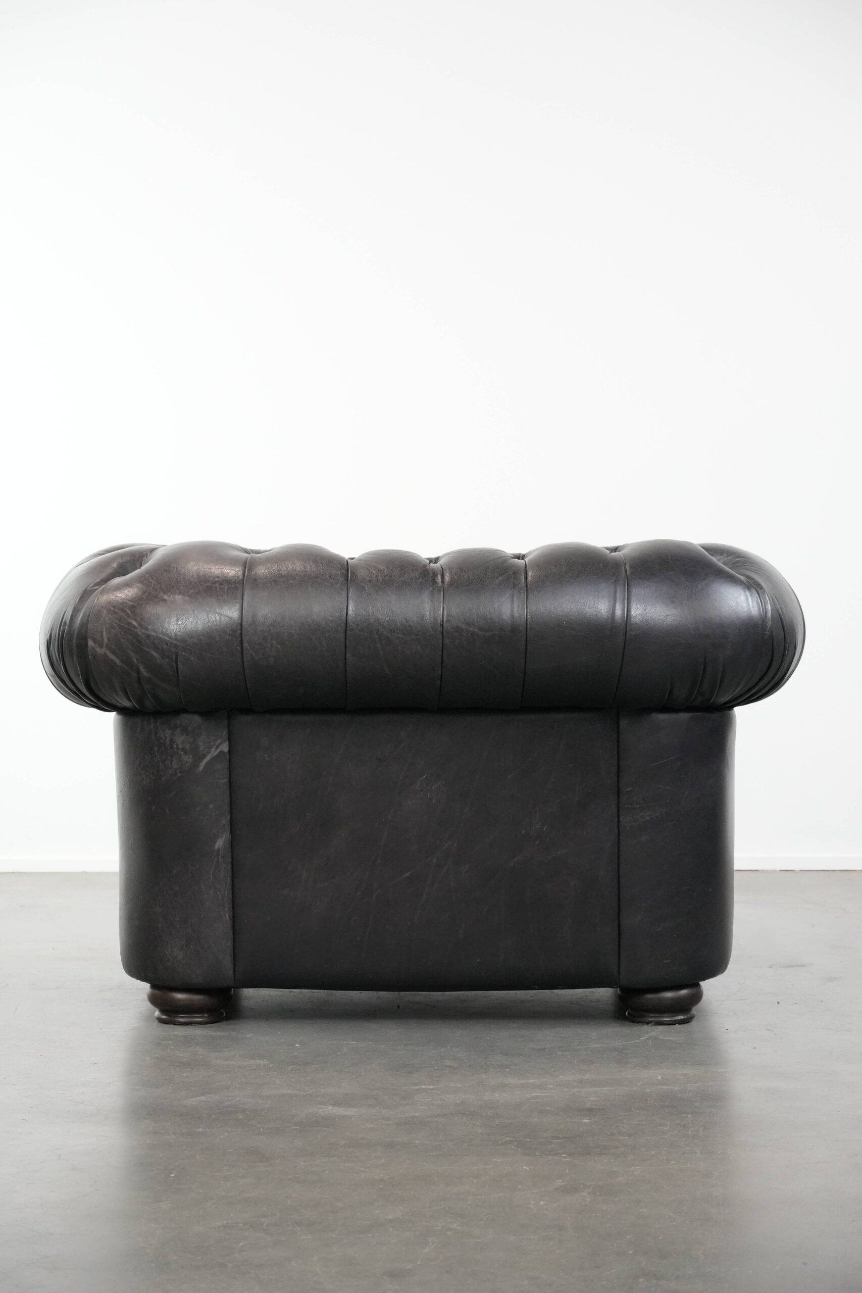 Ensemble composé d'un canapé chesterfield noir, d'un fauteuil et d'un pouf.