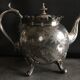 Old teapot pourer in silver metal decorated with foliage and butterflies