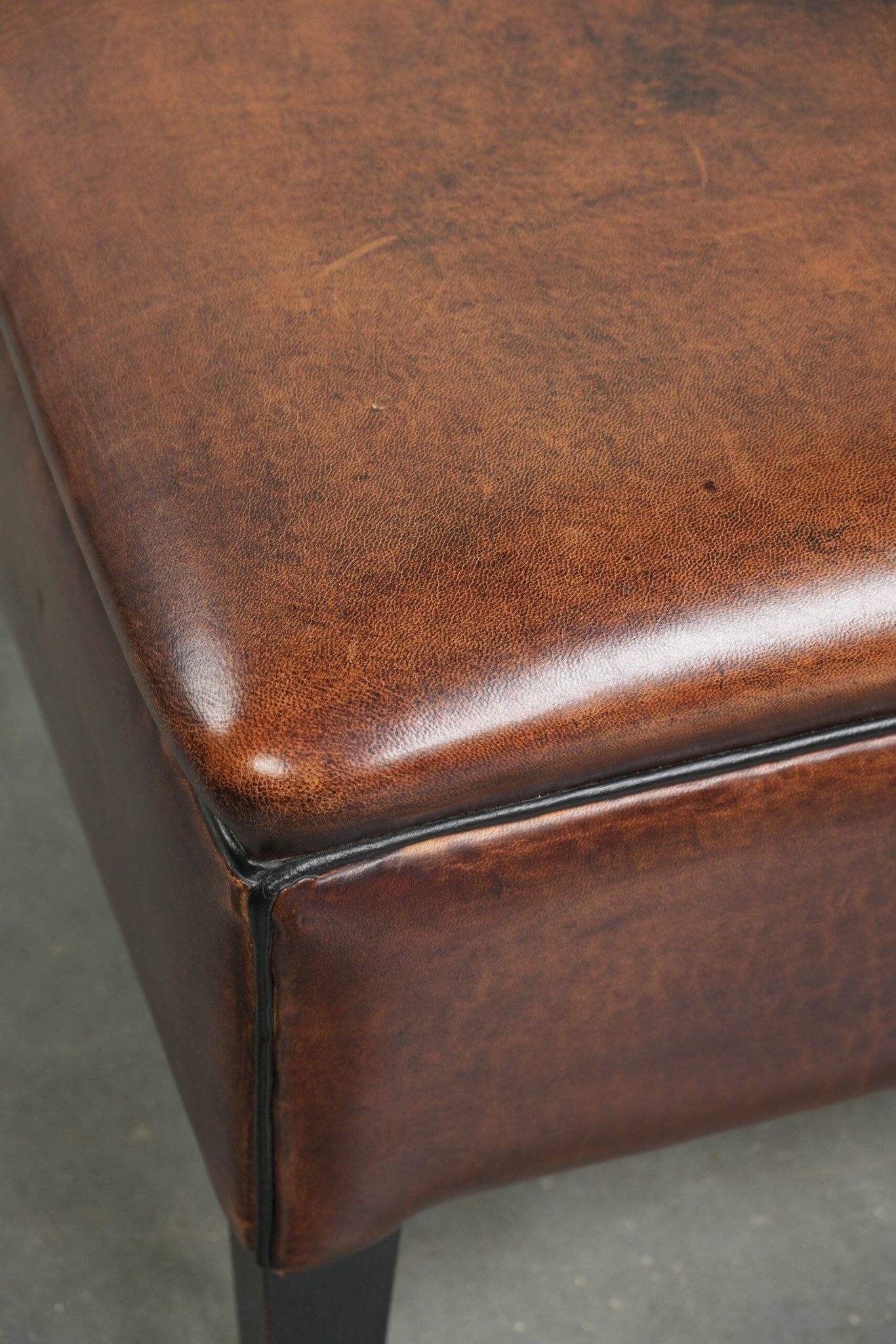 Pouf carré marron foncé en peau de mouton avec un passepoil noir.