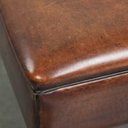 Pouf carré marron foncé en peau de mouton avec un passepoil noir.