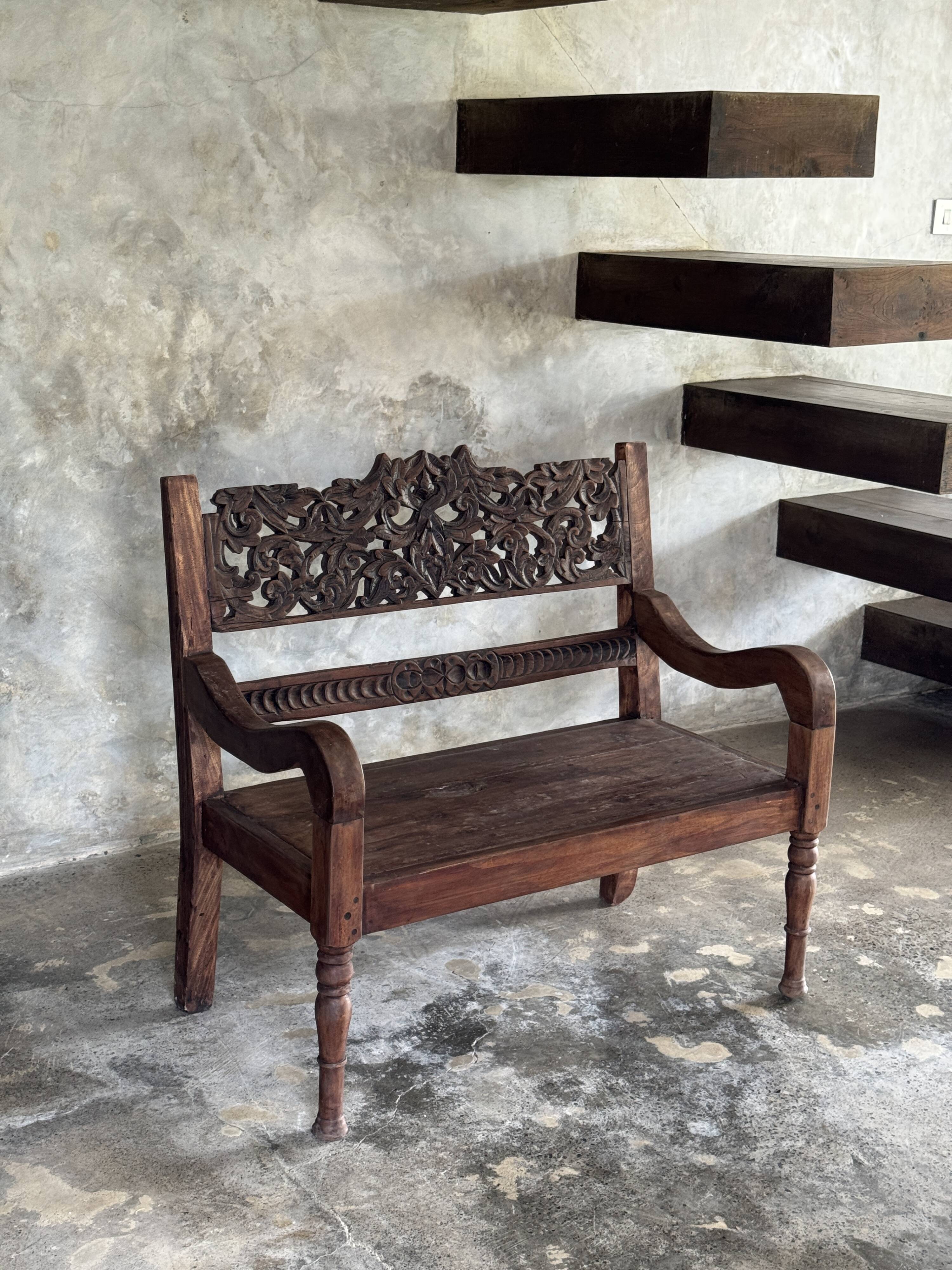Small antique Indonesian bench in carved teak with plant and floral motifs.