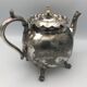 Old teapot pourer in silver metal decorated with foliage and butterflies
