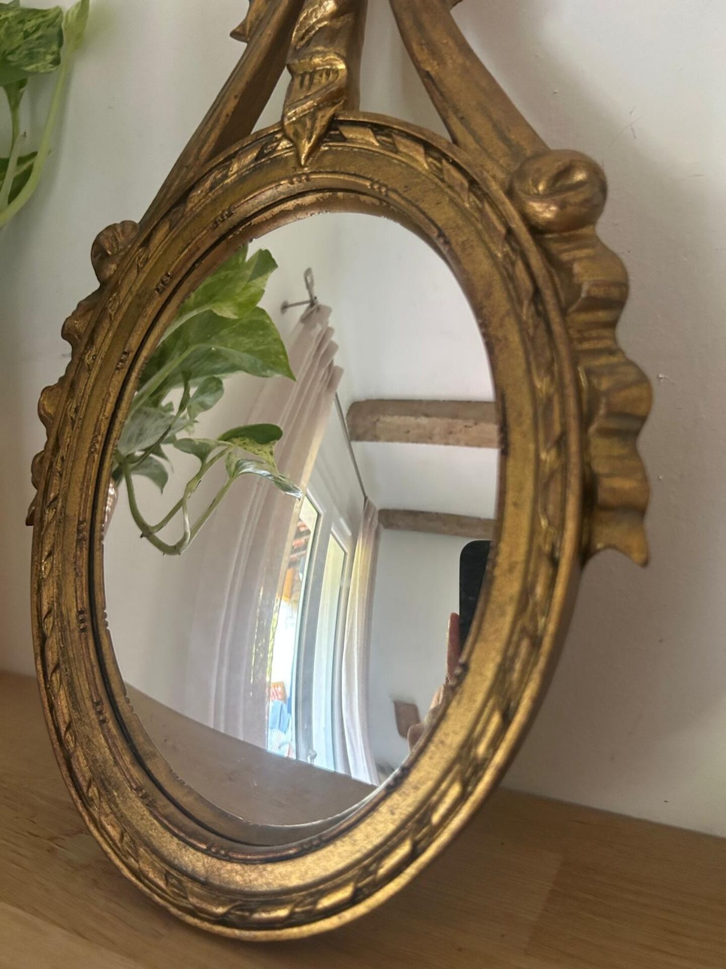 Oval convex witch mirror with golden ribbon mouldings.