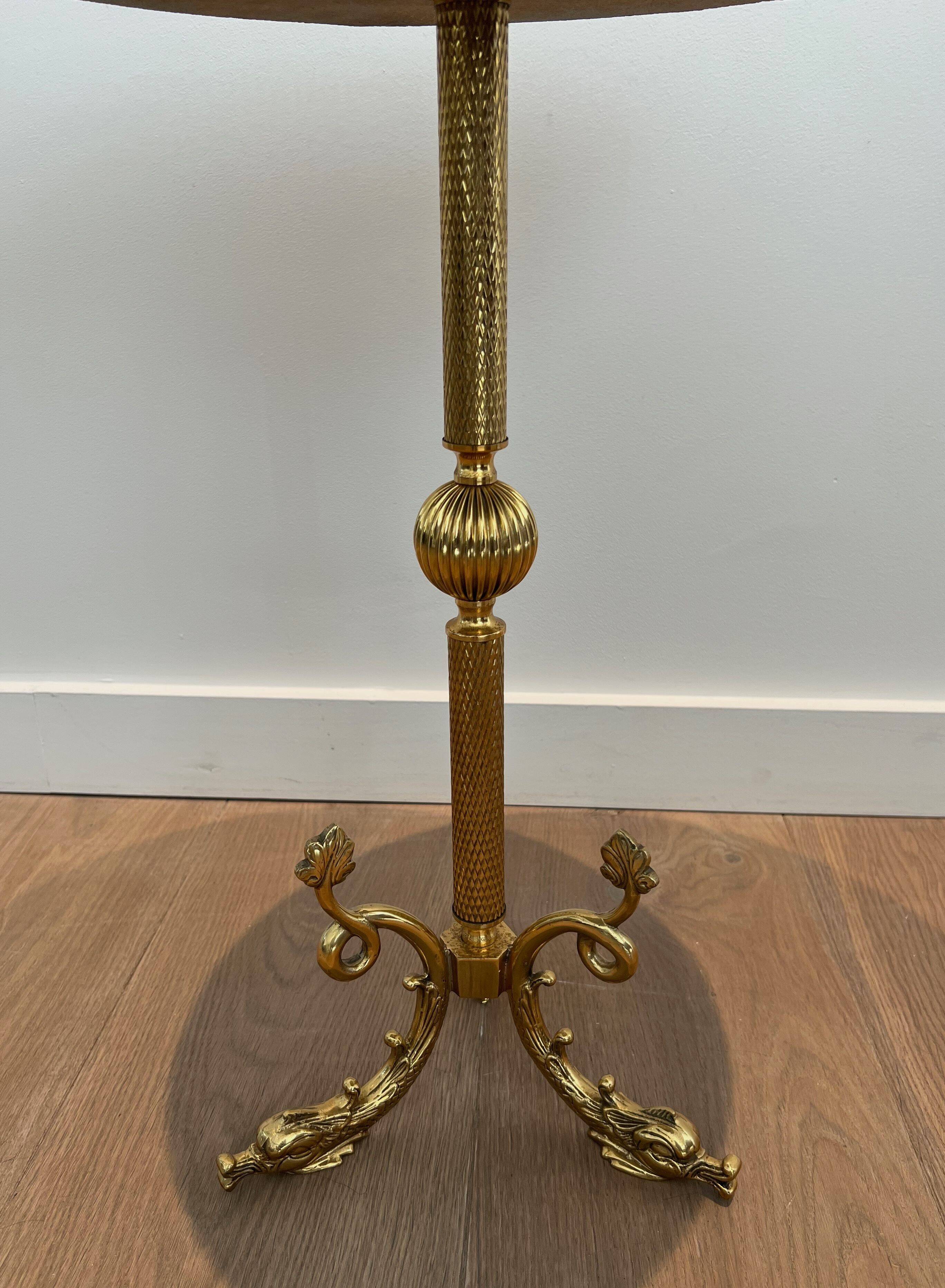 A round, neoclassical-style brass side table with a base decorated with dolphins and a red celluloid top encircled by an openwork gallery, attributed to the House of Jansen.