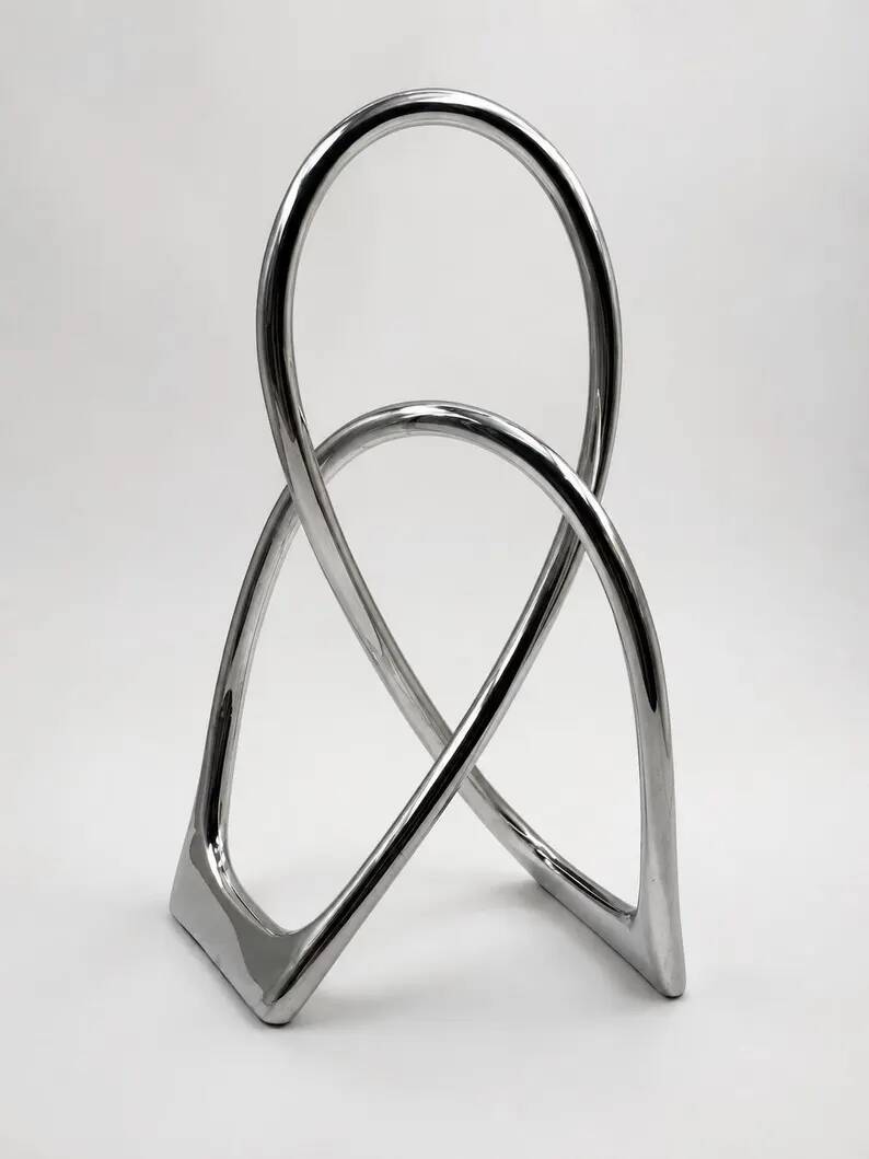 Chromed sculptural art object, abstract modernist shape in metal, contemporary design accent, brutalist interior decoration.