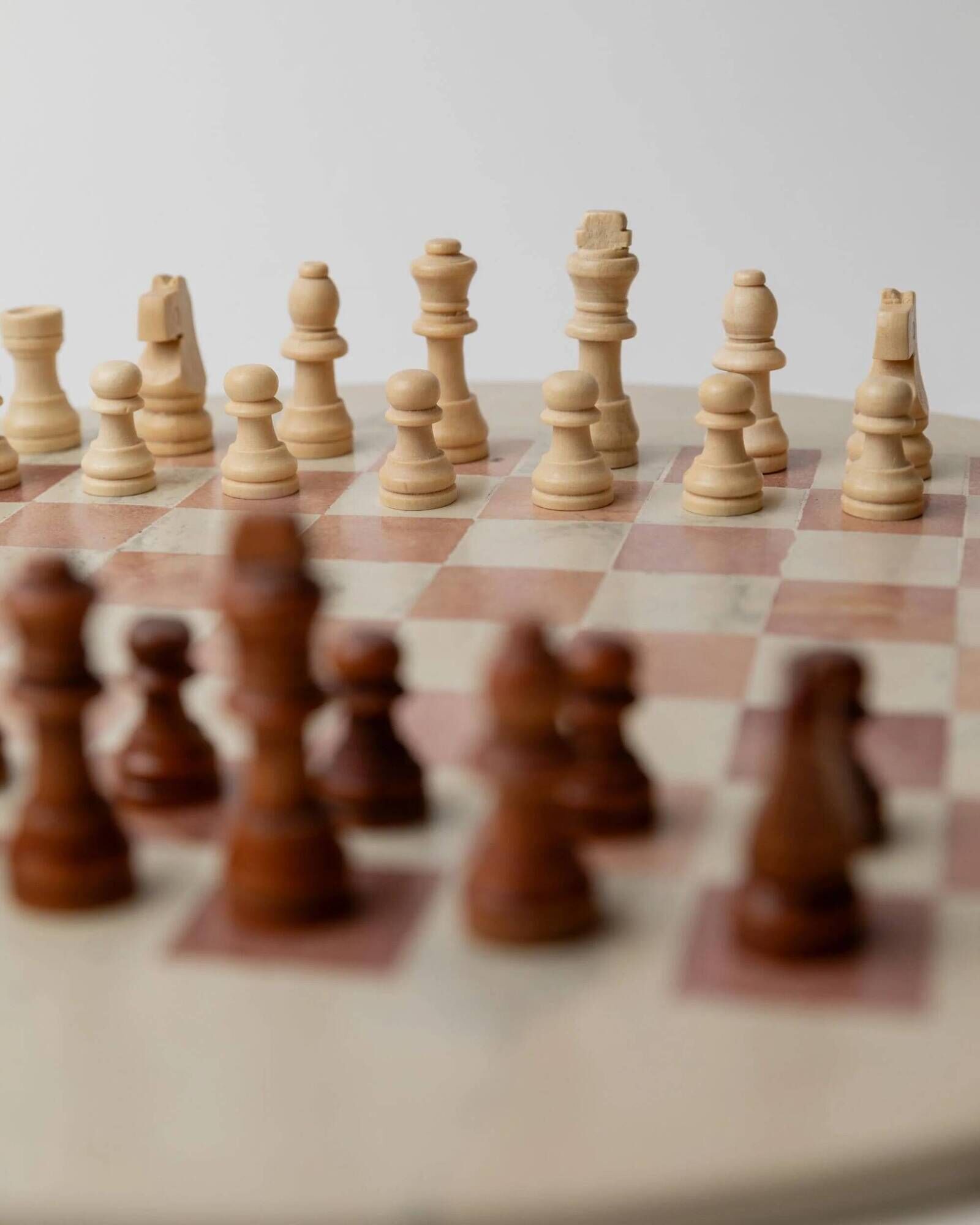 Vintage 1980s round chess set in marble, with a beige and pink marble board and wooden pieces.