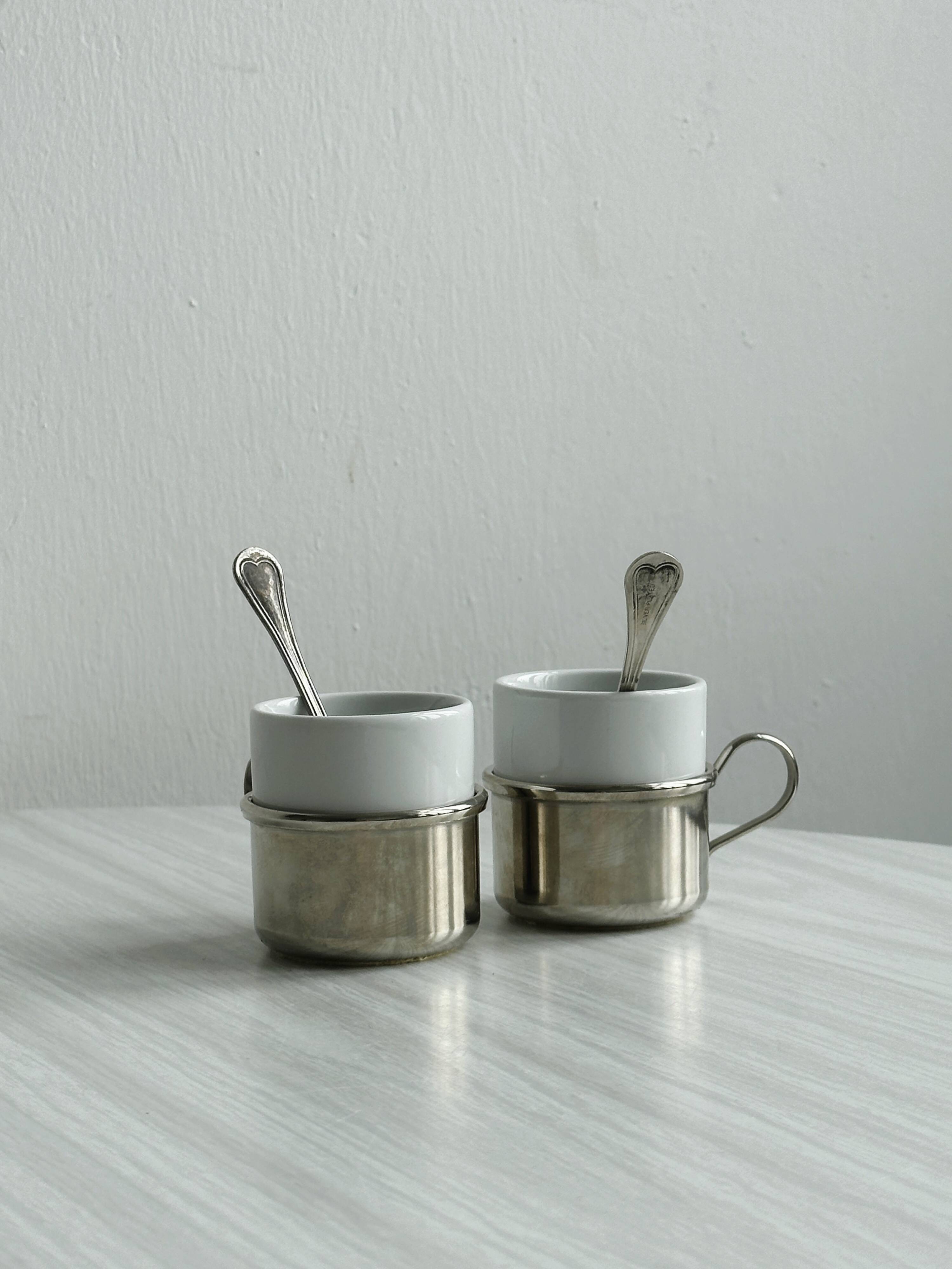 2 porcelain cups with metal supports and small spoons.