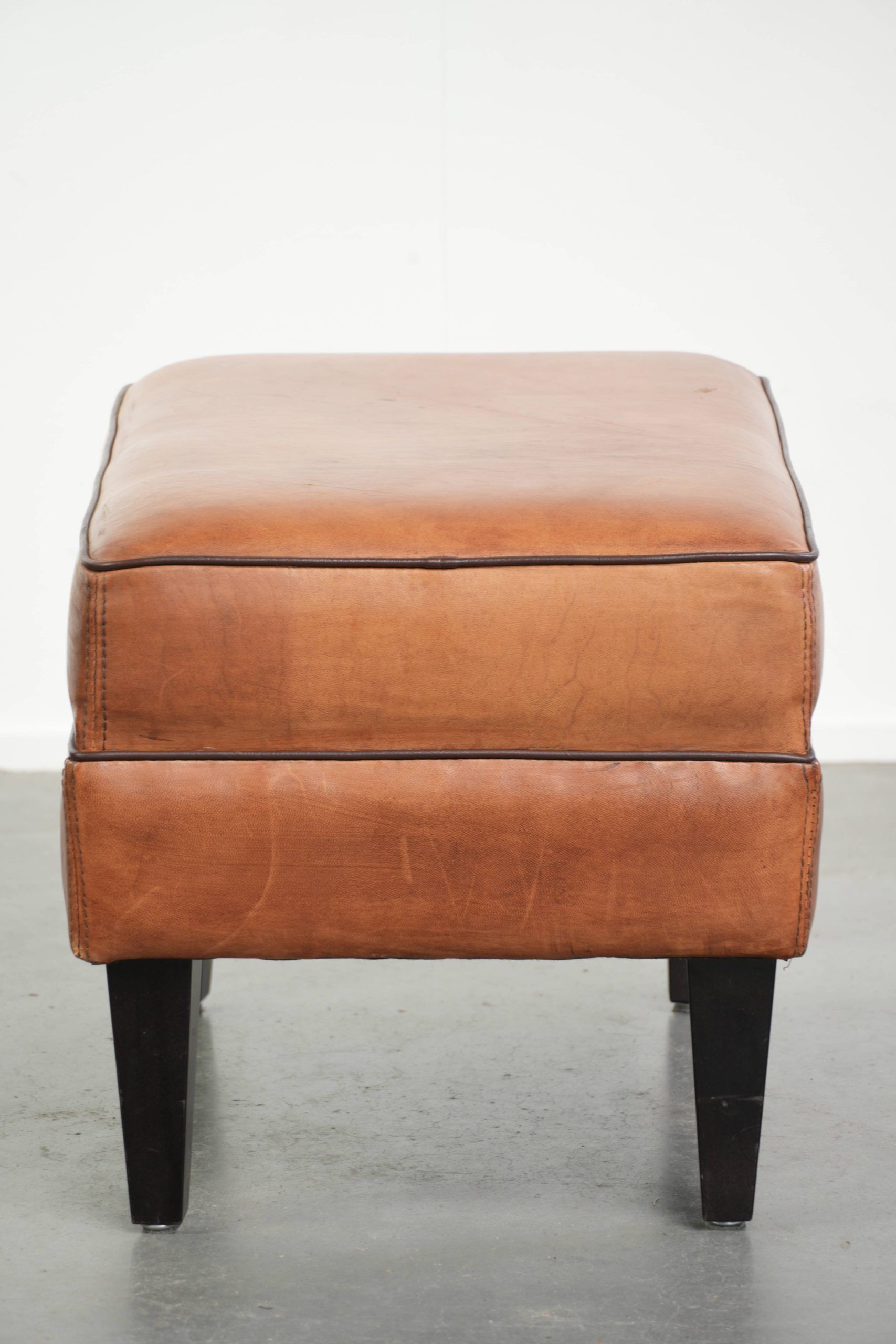 Handy sheepskin ottoman with warm colours finished with black piping
