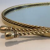Oval brass mirror surrounded by a cord and adorned