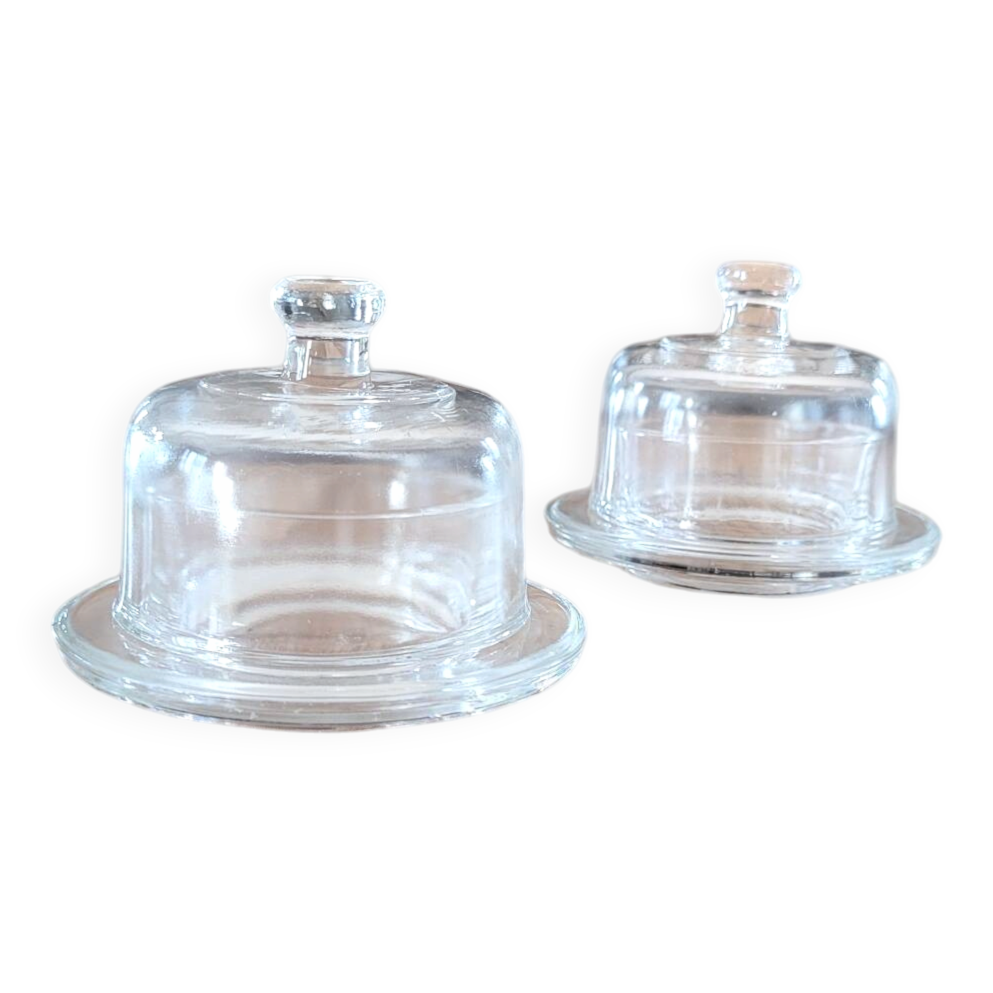 2 transparent glass butter dishes accompanied by their matching cloches.