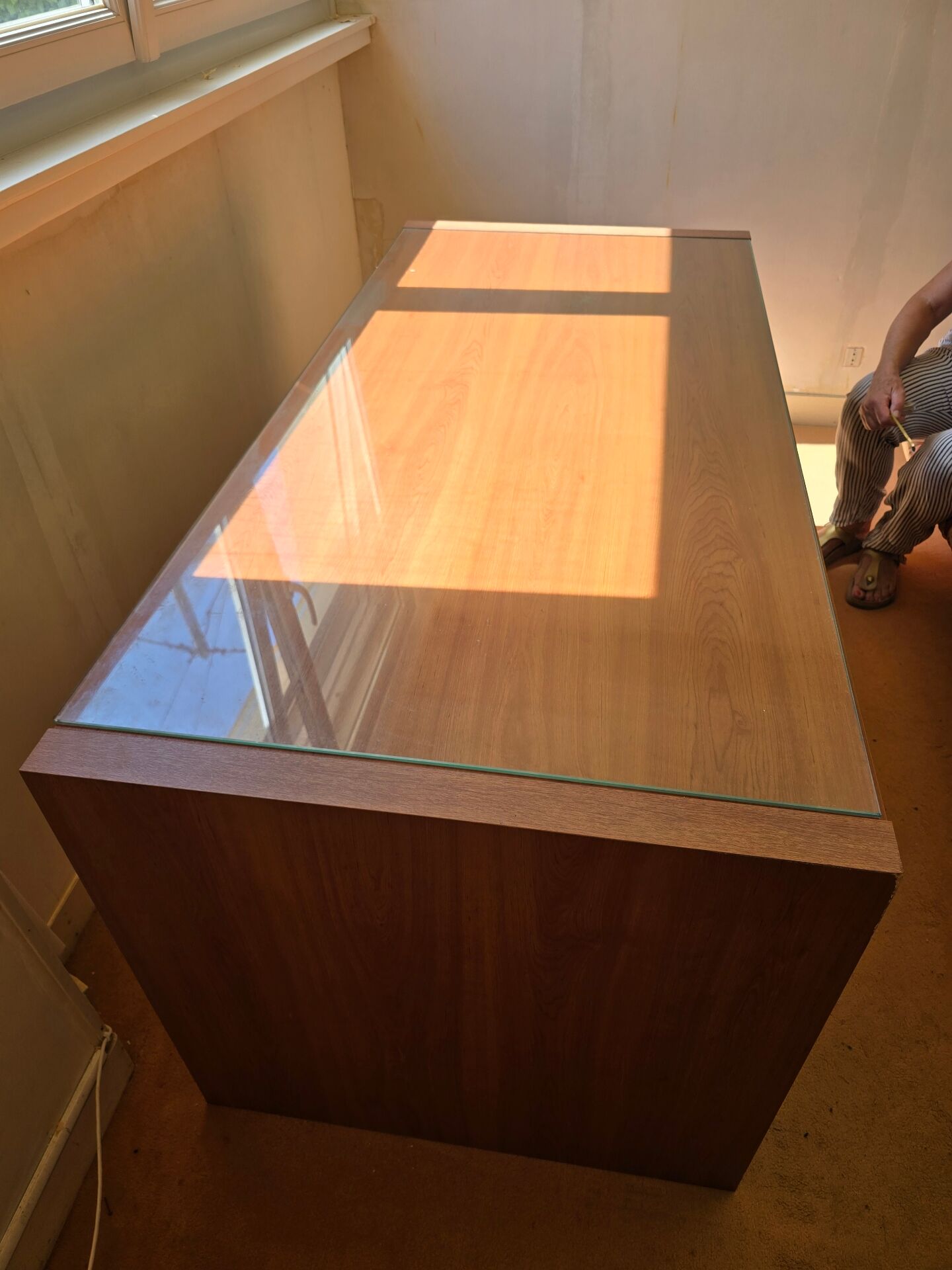 Large wooden desk with a glass top and a wheeled drawer unit.