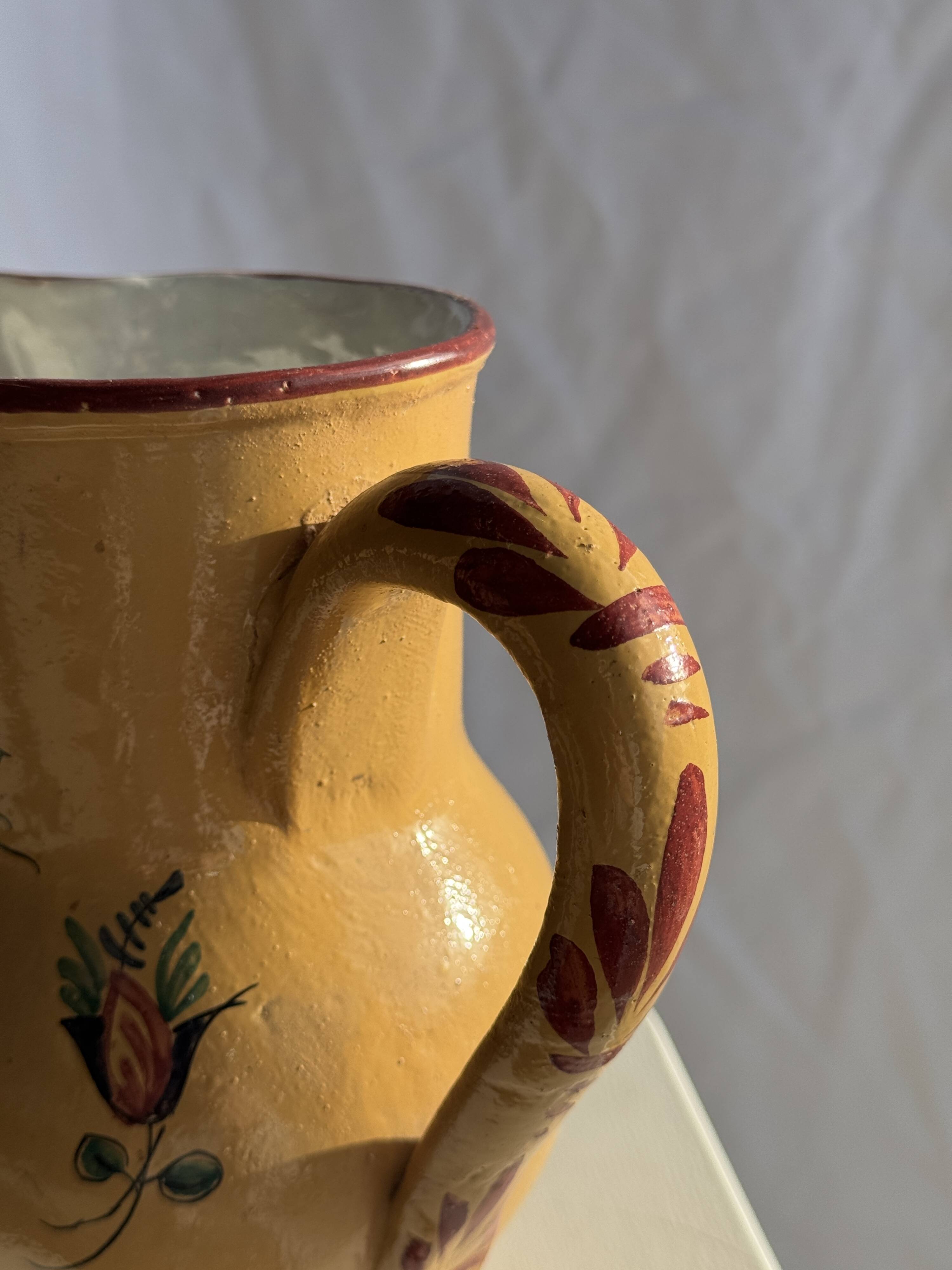 Large antique handmade ochre yellow jug with a pink flower pattern.