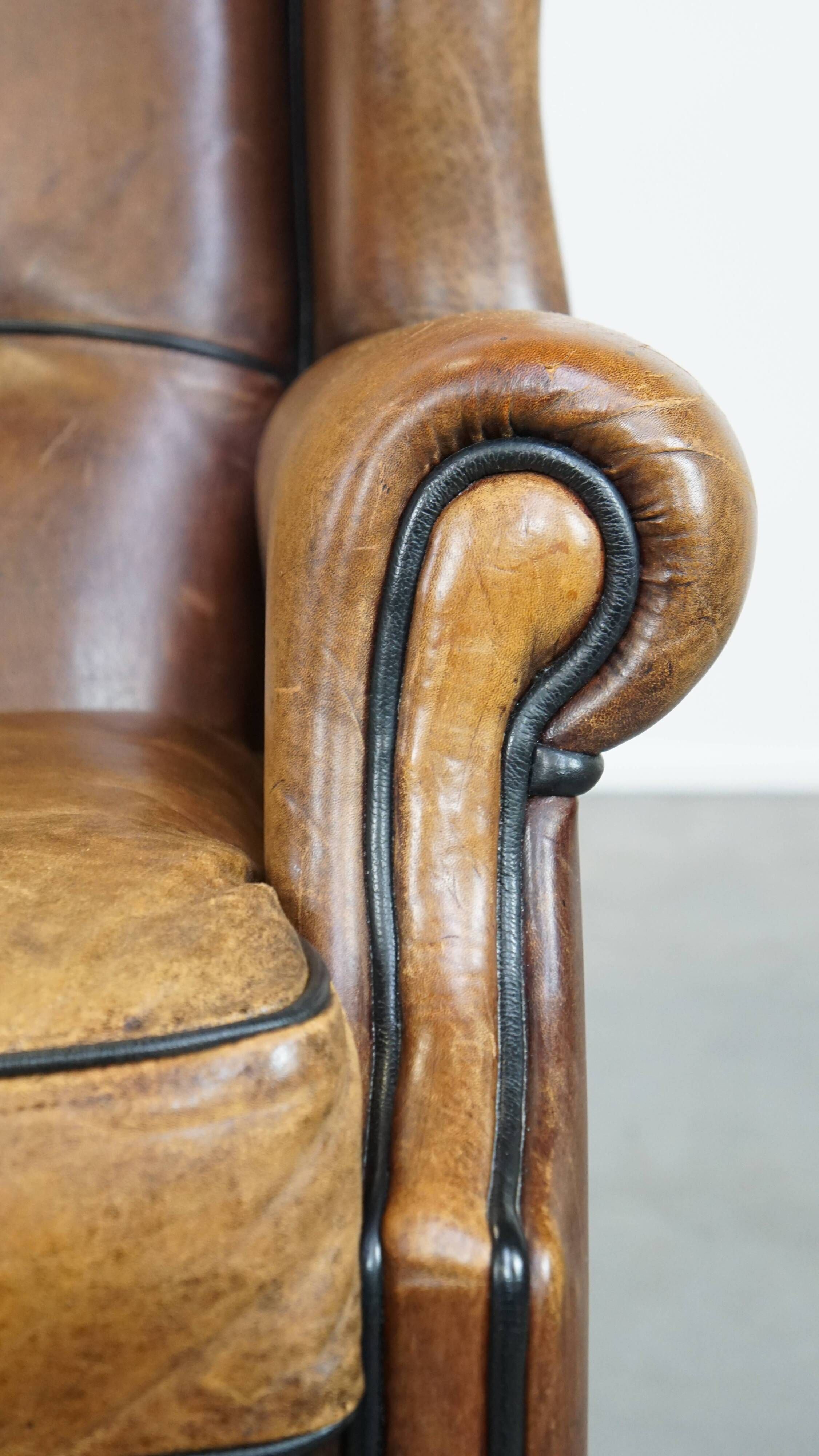 Cognac-colored sheep leather wingback chair finished with black piping