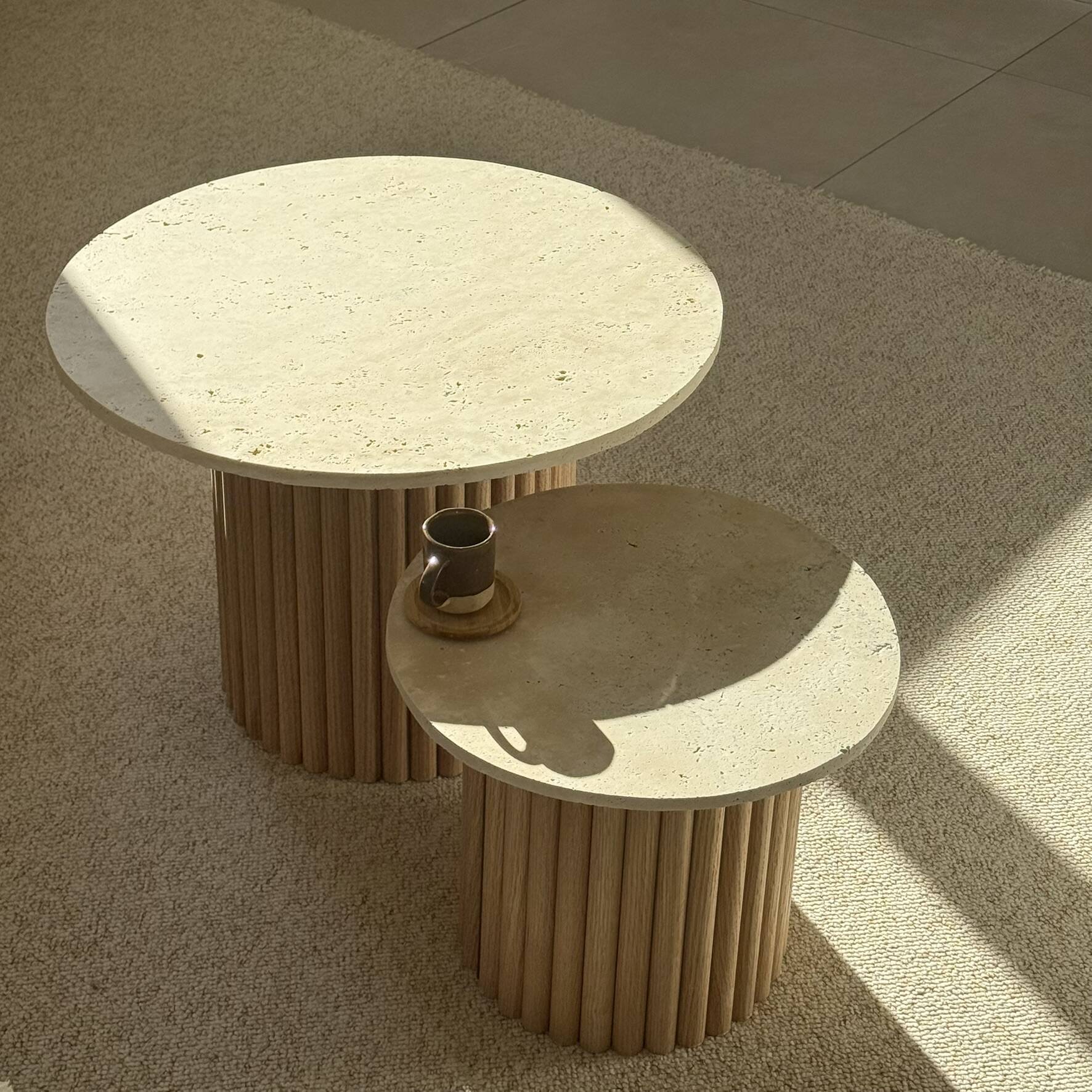 Round nesting coffee table in travertine and raw fluted wood.