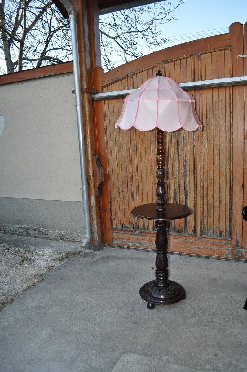 Brown carved wooden floor lamp with a pale pink shade and integrated shelf.