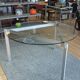 Round dining table with a glass top and brushed metal triangular frame.