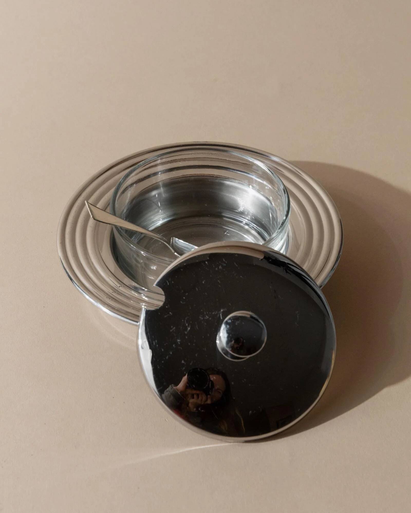 Vintage 1970s condiment pot made of glass and stainless steel with a lid, complete with a matching spoon.
