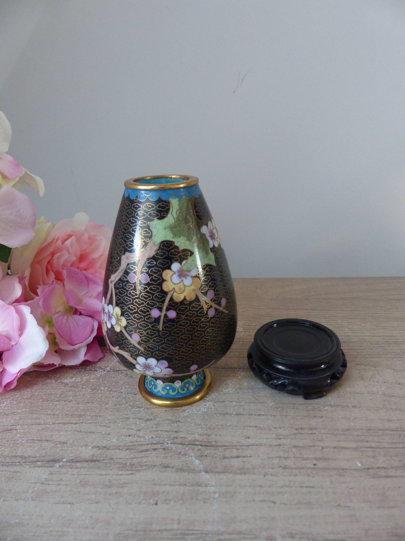 Small black cloisonné vase decorated with yellow and pink cherry blossoms, vase on wooden base