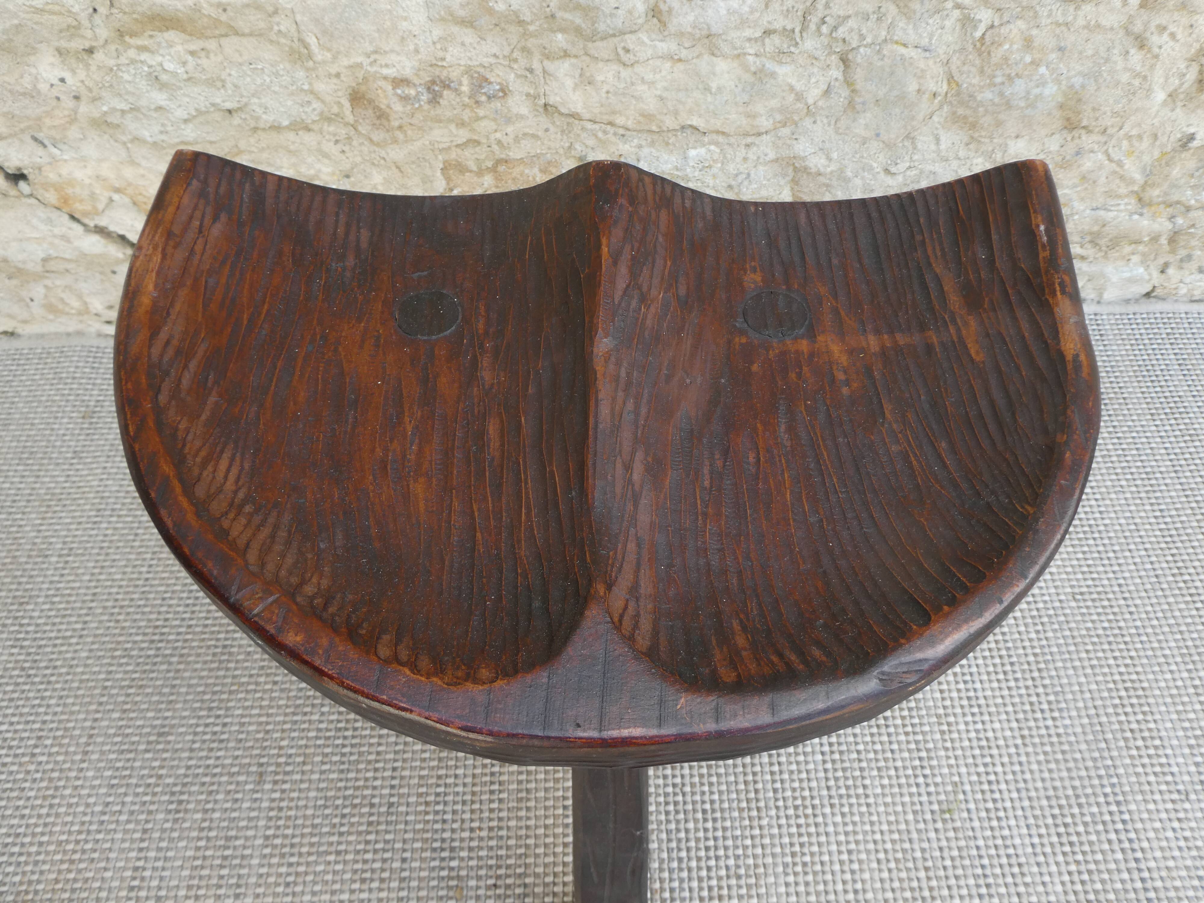 Tripod stool made of solid wood, with a carved seat.
