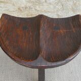 Tripod stool made of solid wood, with a carved seat.