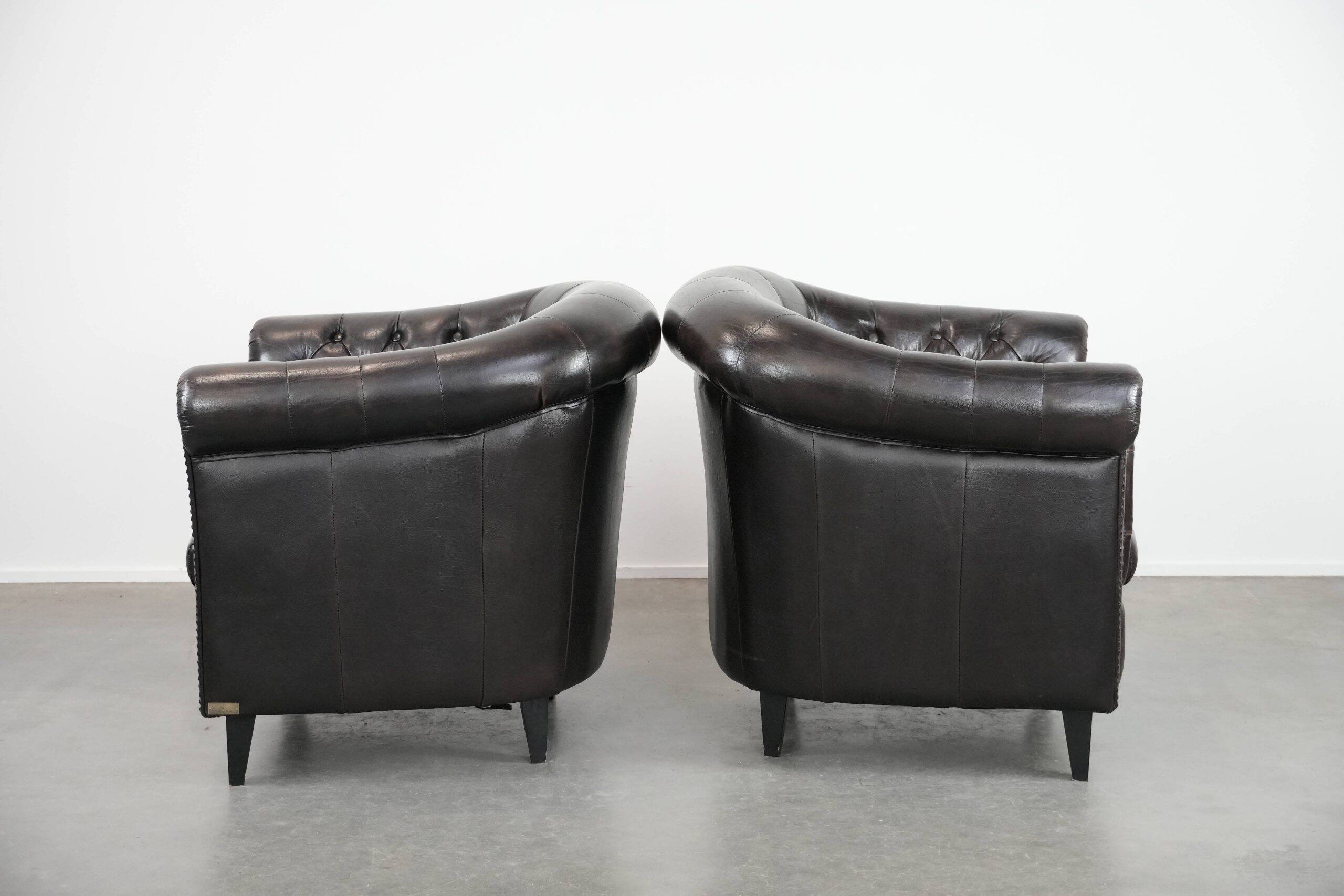 Ensemble de deux luxueux fauteuils club Chesterfield en cuir de vachette noir.