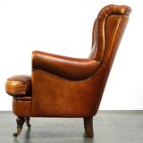 Subtle sheepskin wing chair in good condition on brass front wheels