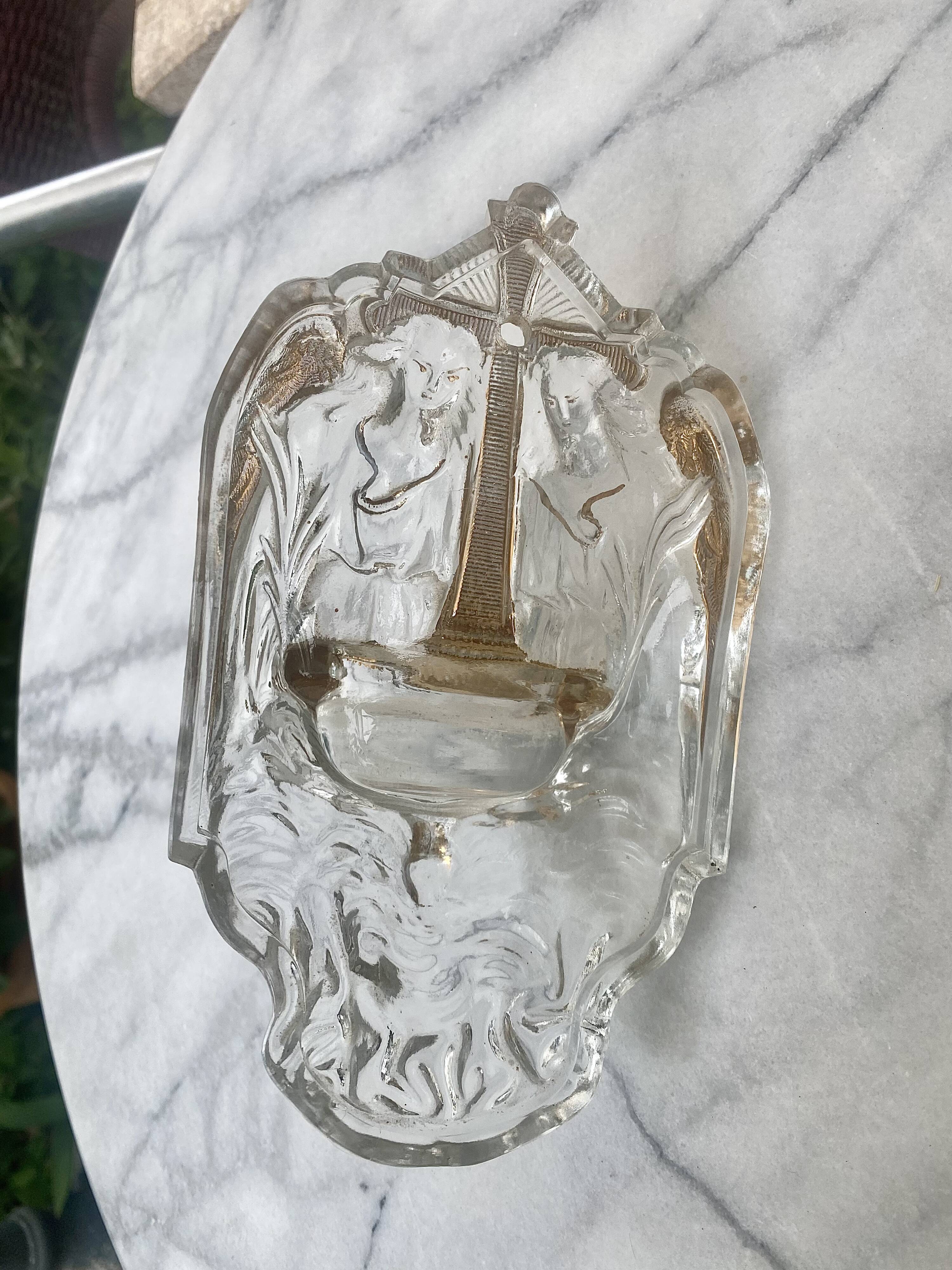 Old wall-mounted holy water font in moulded glass decorated with angels.