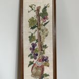 Broderie hollandaise encadrée représentant une vigne avec des raisins, des bouteilles de vin et des paniers