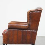 Sheep leather wingback chair with a red corduroy seat cushion and patina