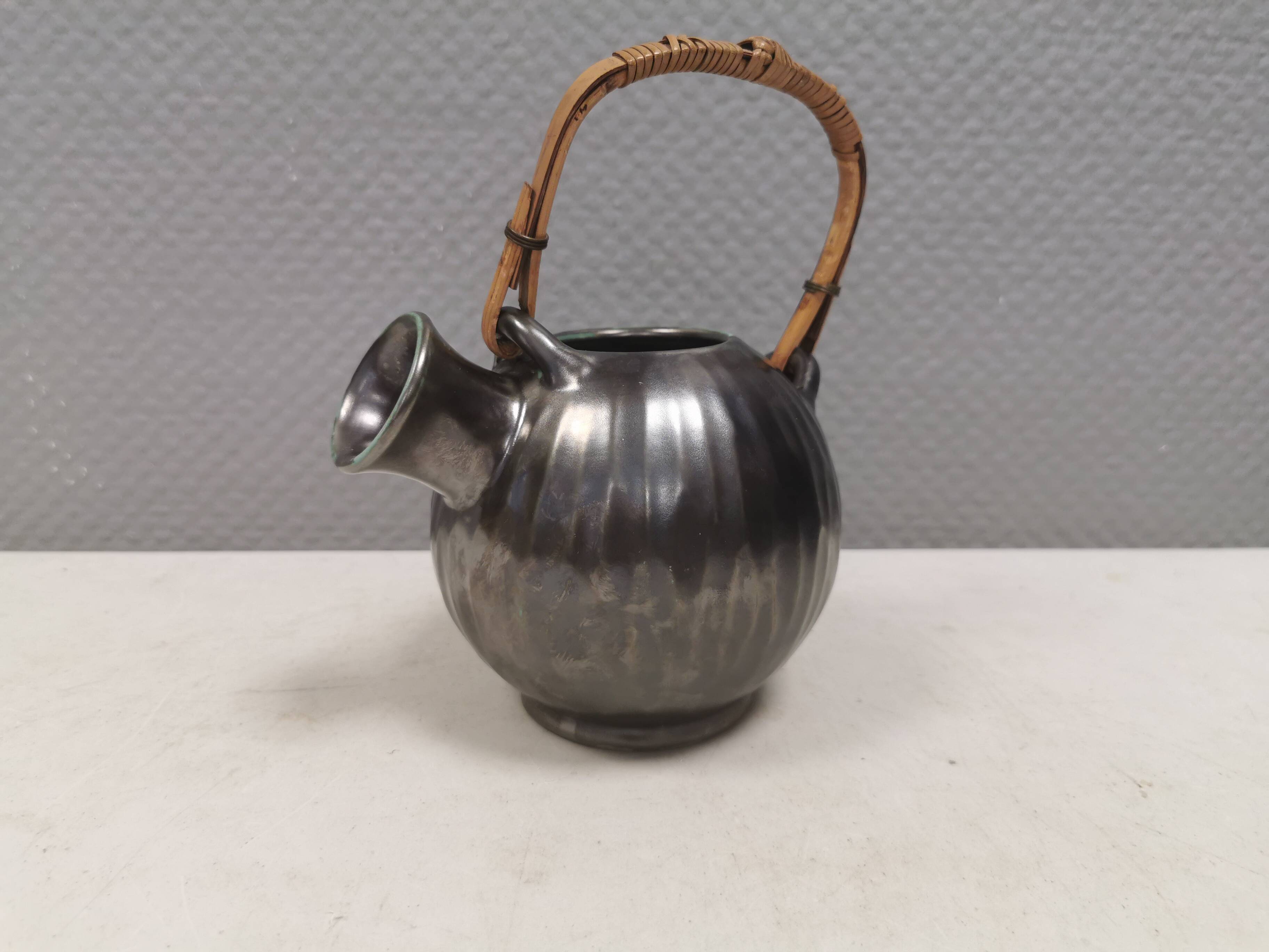 A ceramic jug with a metallic glaze and a handle made of woven raffia.