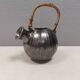 A ceramic jug with a metallic glaze and a handle made of woven raffia.