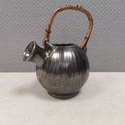 A ceramic jug with a metallic glaze and a handle made of woven raffia.
