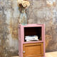 Pink bedside table with haberdashery and raw wood.