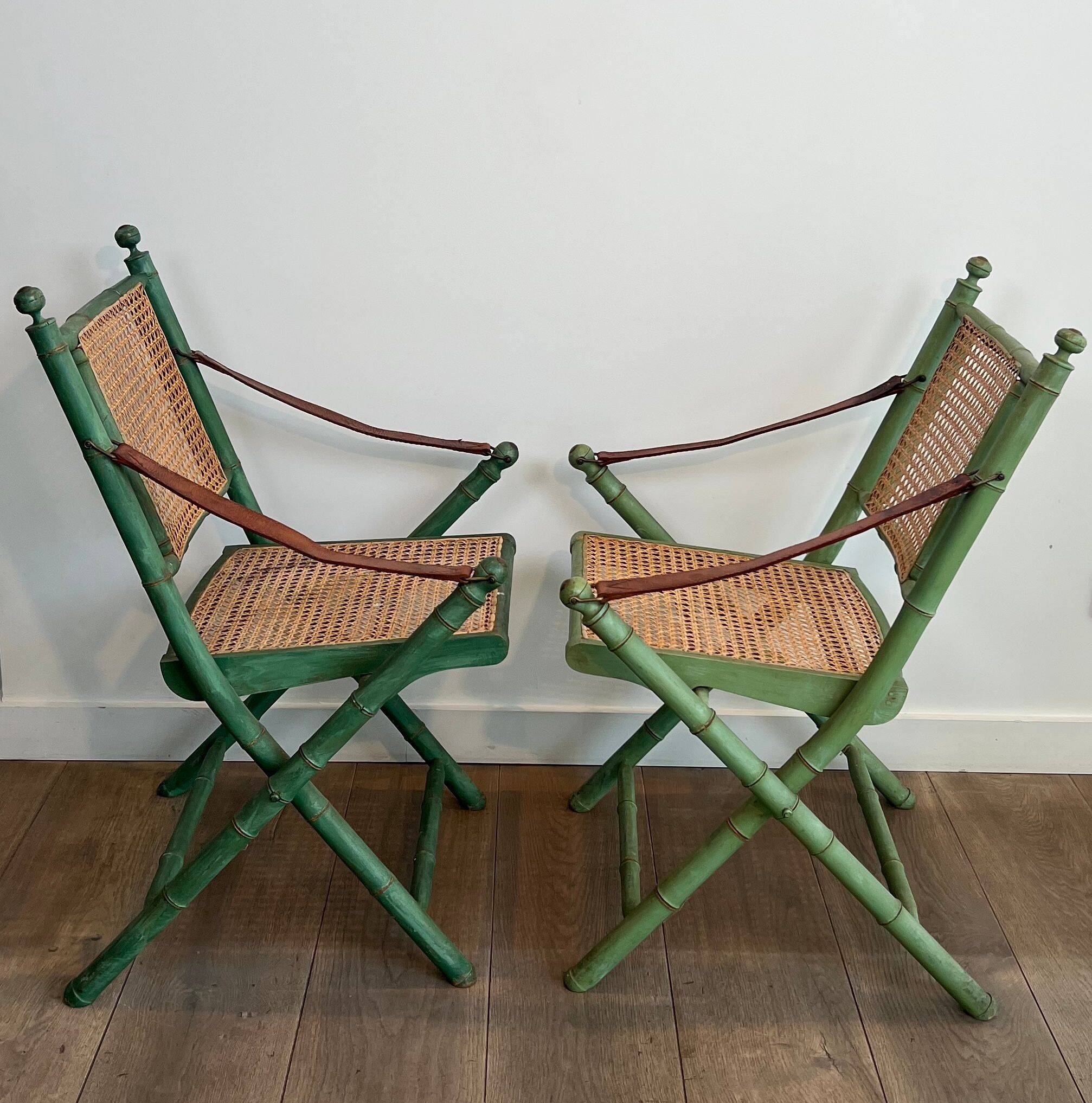 Paire de chaises safari pliantes façon faux-bambou patiné, dossiers et assises cannées et repose-bras en cuir